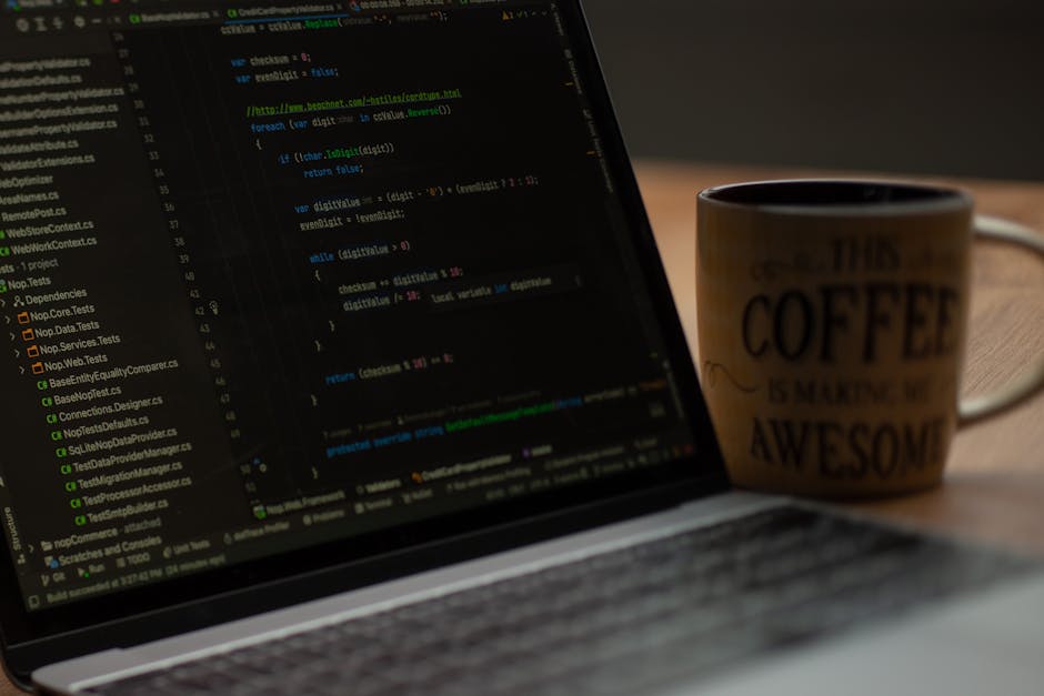 Close-up of a person's hands working on a laptop with a dark-themed code editor displayed on the screen, showing lines of programming code with colored syntax highlighting. The laptop is placed on a d